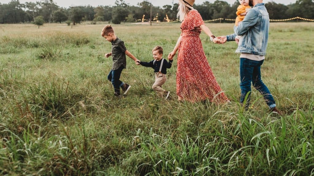Family with kids walking through grassy field with string lights, warm community gathering