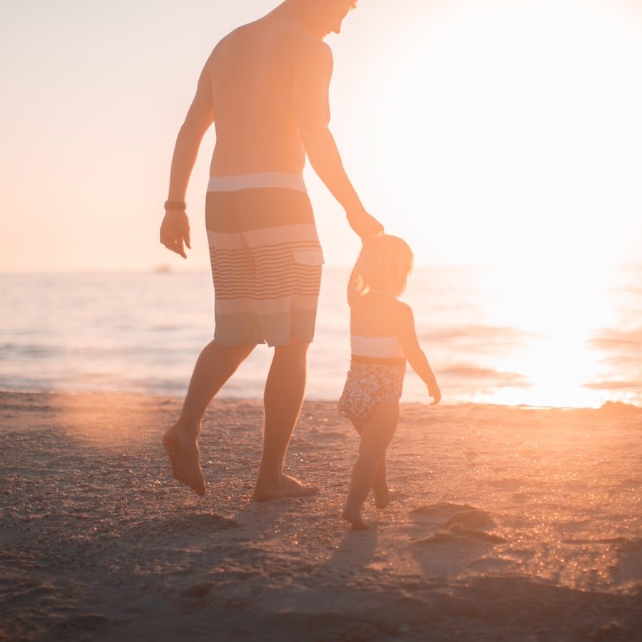 Father and young child walking on beach at sunset, family parenting